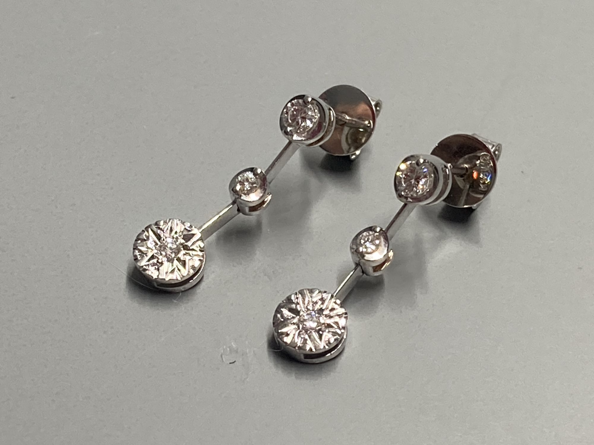 A modern pair of 18ct white gold and illusion set three stone diamond drop earrings, 19mm, gross 2.3 grams.